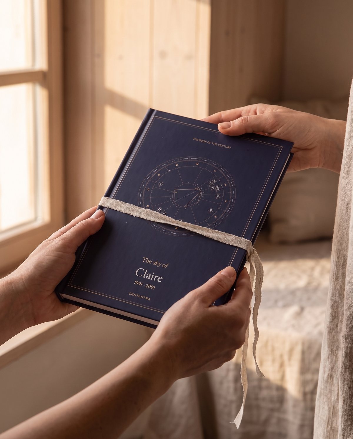 The Centastra book, navy cover with its celestial chart, tied with a ribbon, resting on linen