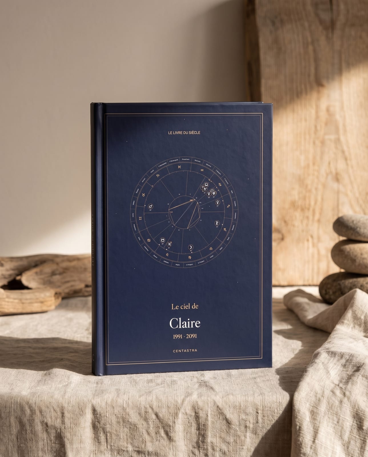 Le livre Centastra relié rigide, couverture bleu nuit à la carte céleste, posé sur un lin ivoire